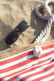 Stylish sunglasses and beach bag on sand, above view