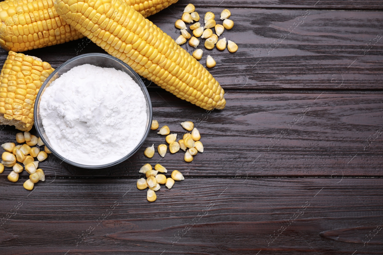 Photo of Bowl with corn starch, ripe cobs and kernels on dark wooden table, flat lay. Space for text