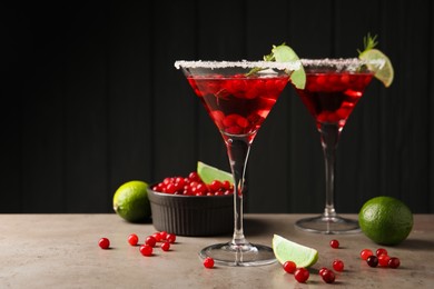 Photo of Tasty cranberry cocktail with rosemary and lime in glasses on grey table against black background, space for text