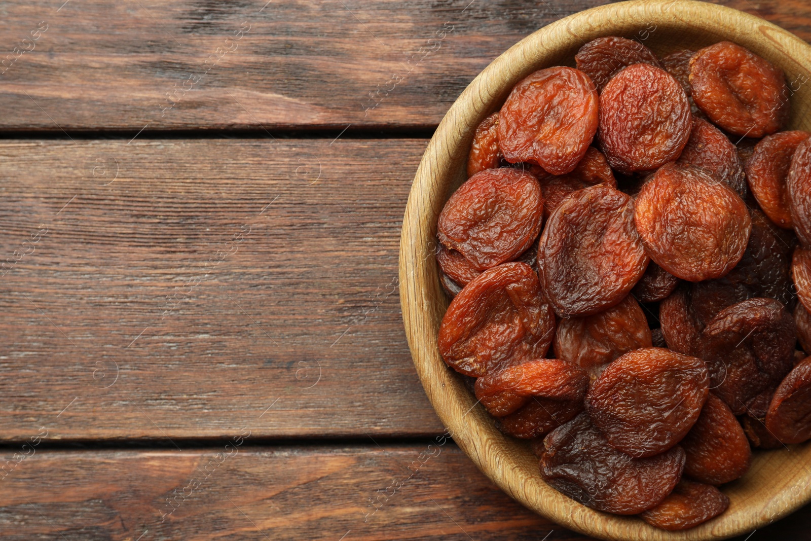 Photo of Bowl of tasty apricots on wooden table, top view and space for text. Dried fruits