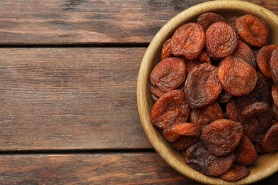 Photo of Bowl of tasty apricots on wooden table, top view and space for text. Dried fruits