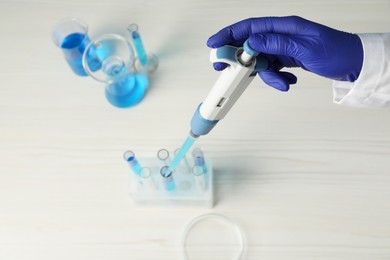 Photo of Laboratory analysis. Scientist dripping sample with micropipette into test tube at white wooden table, above view