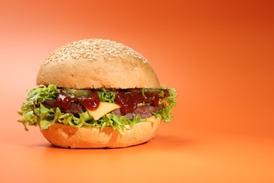 Photo of Delicious cheeseburger with lettuce, pickle, ketchup and patty on coral background. Space for text