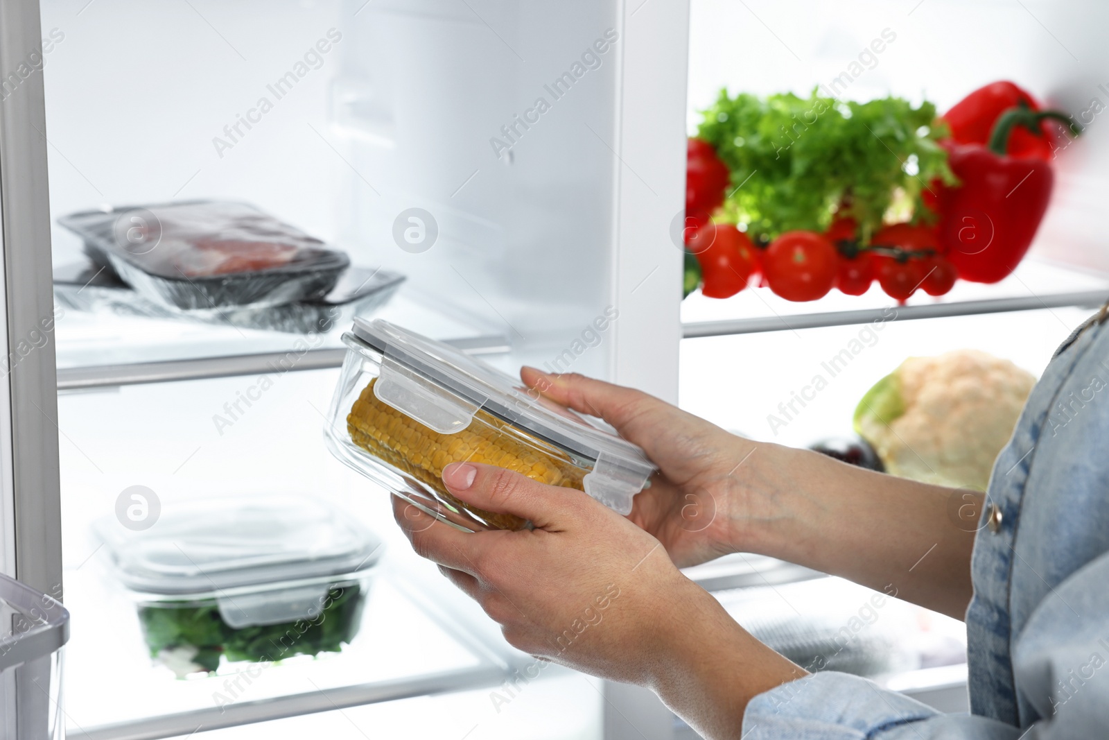 Photo of Young woman taking container with corn out of refrigerator, closeup