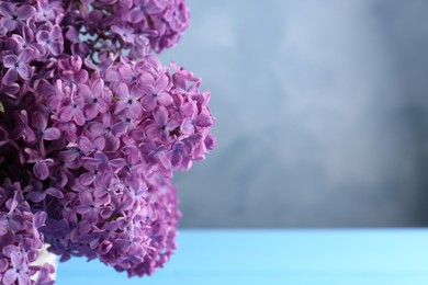 Photo of Beautiful lilac flowers in wicker basket near blue wall, closeup. Space for text