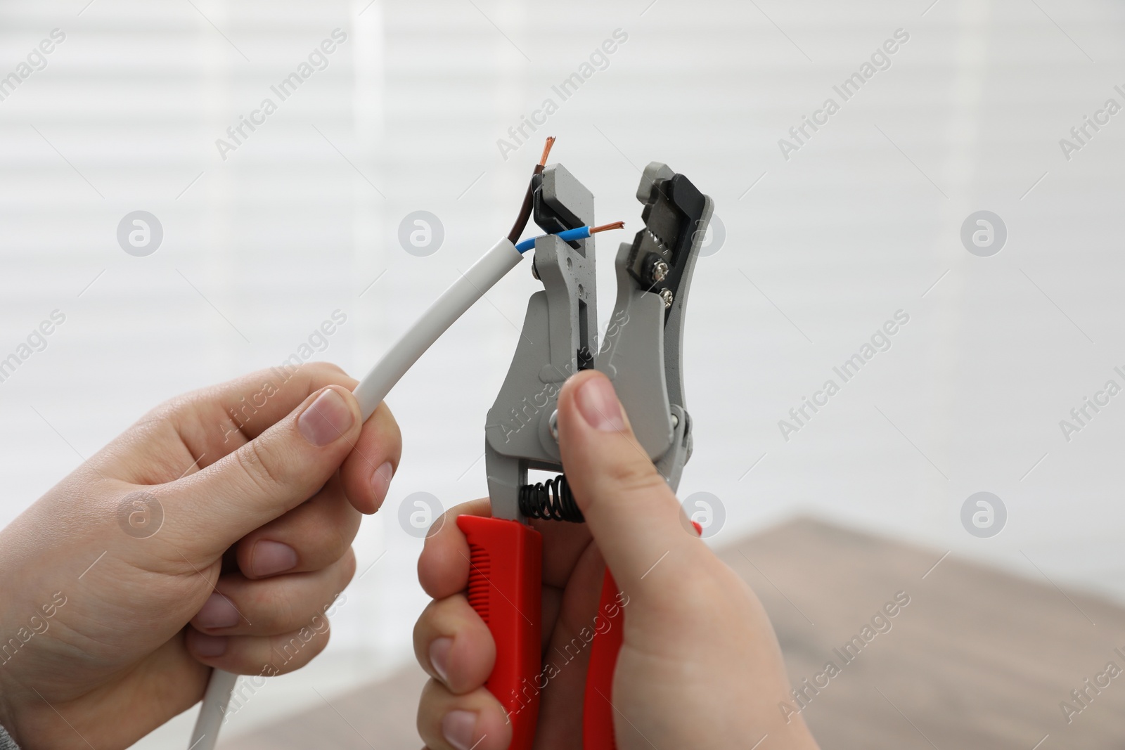 Photo of Professional electrician stripping wiring indoors, closeup view