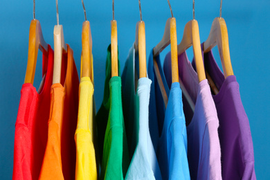 Photo of Bright clothes on wooden hangers against blue background. Rainbow colors