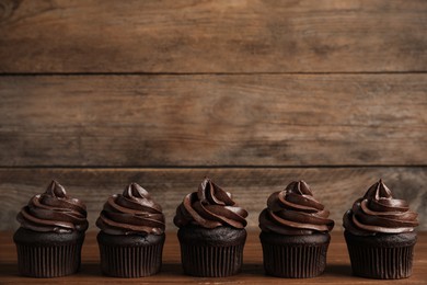 Photo of Delicious chocolate cupcakes with cream on wooden table. Space for text