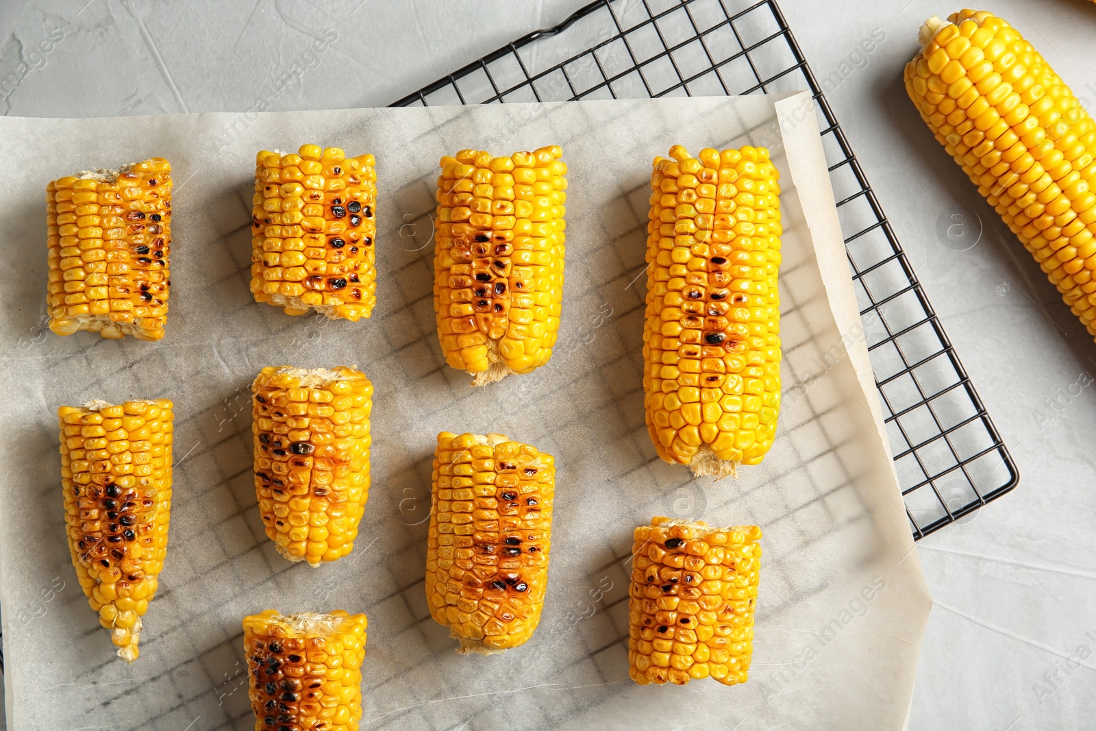 Photo of Cooling rack with grilled corn cobs on light background, top view