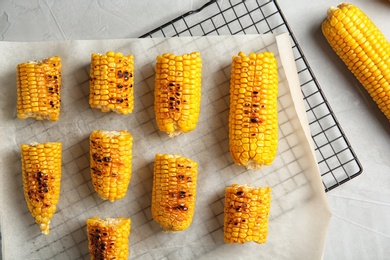 Cooling rack with grilled corn cobs on light background, top view