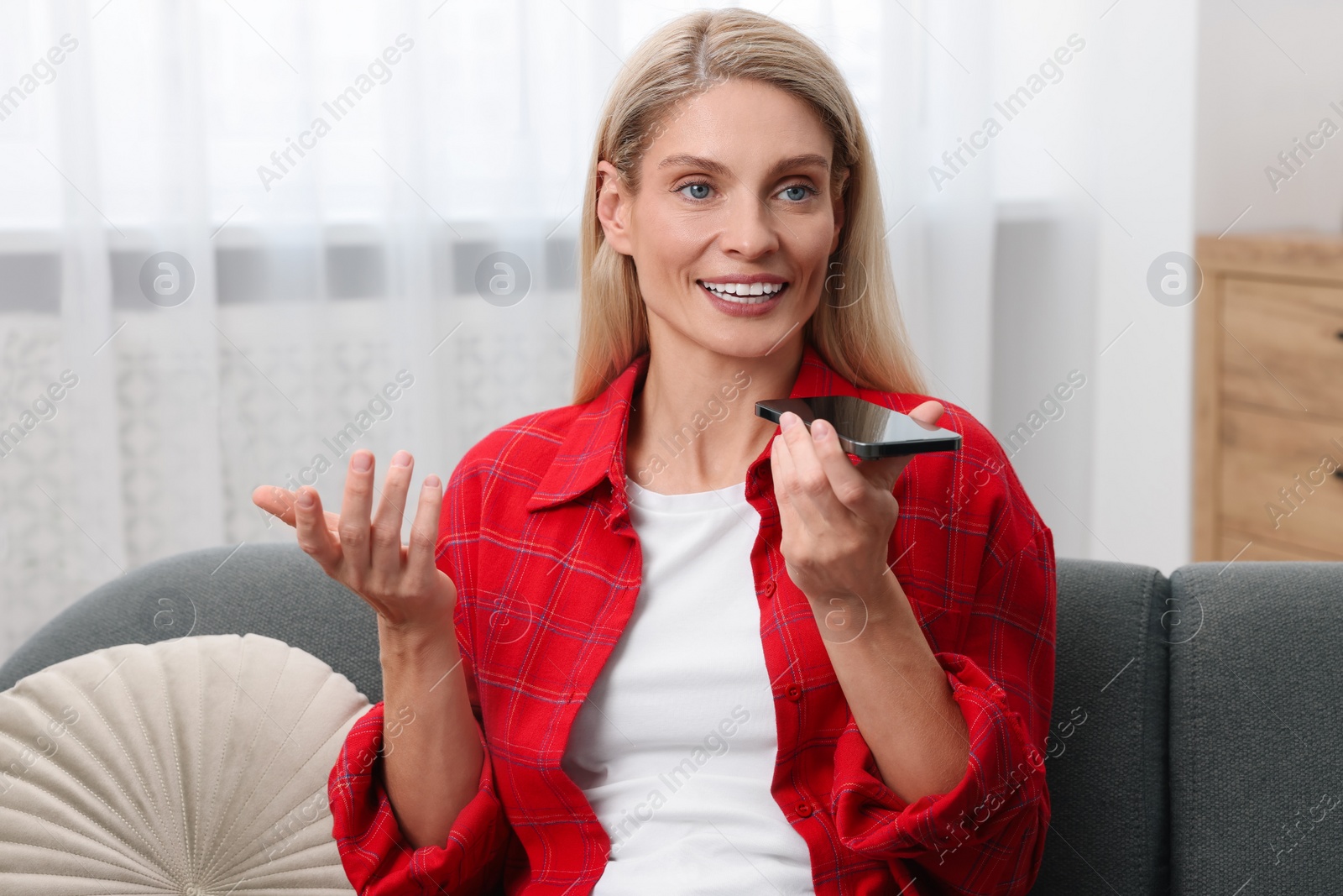 Photo of Woman recording voice message via smartphone on couch at home