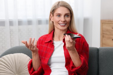 Photo of Woman recording voice message via smartphone on couch at home