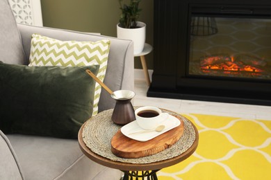 Photo of Cup of coffee and cezve on table near fireplace in living room