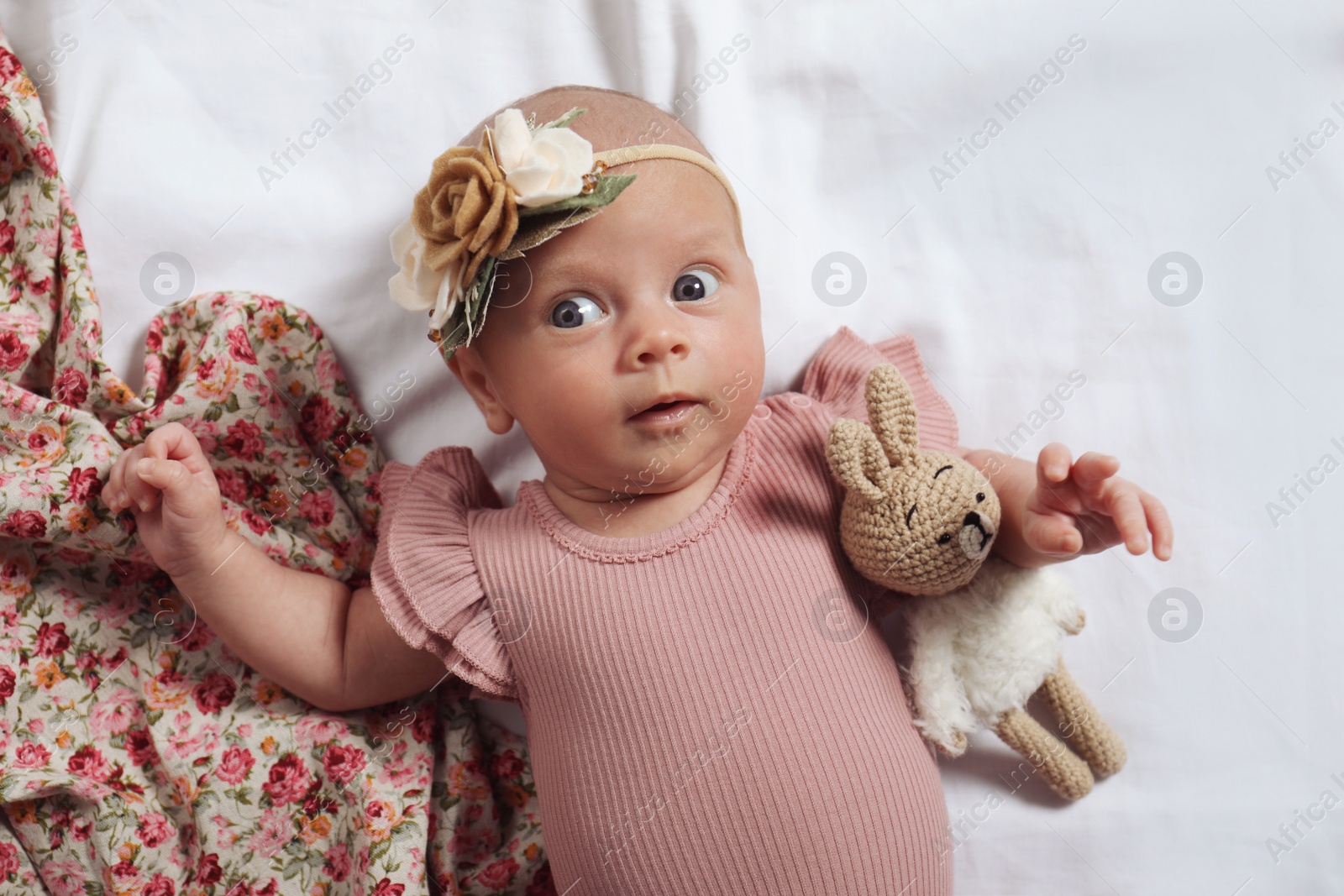 Photo of Cute newborn baby girl with floral headband on bed, top view