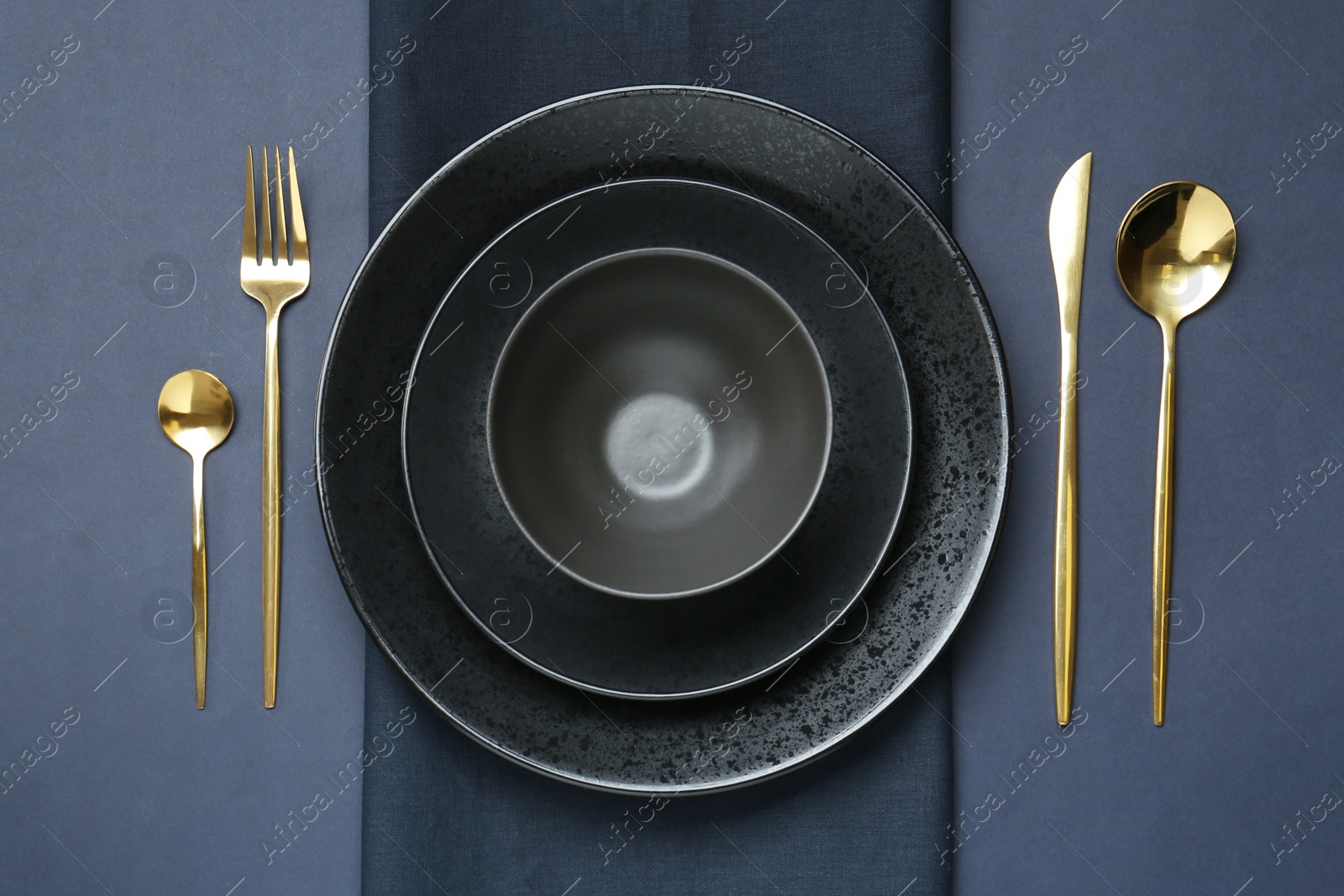 Photo of Stylish ceramic plates, bowl, cutlery and napkin on dark blue background, flat lay