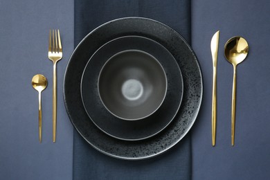 Stylish ceramic plates, bowl, cutlery and napkin on dark blue background, flat lay