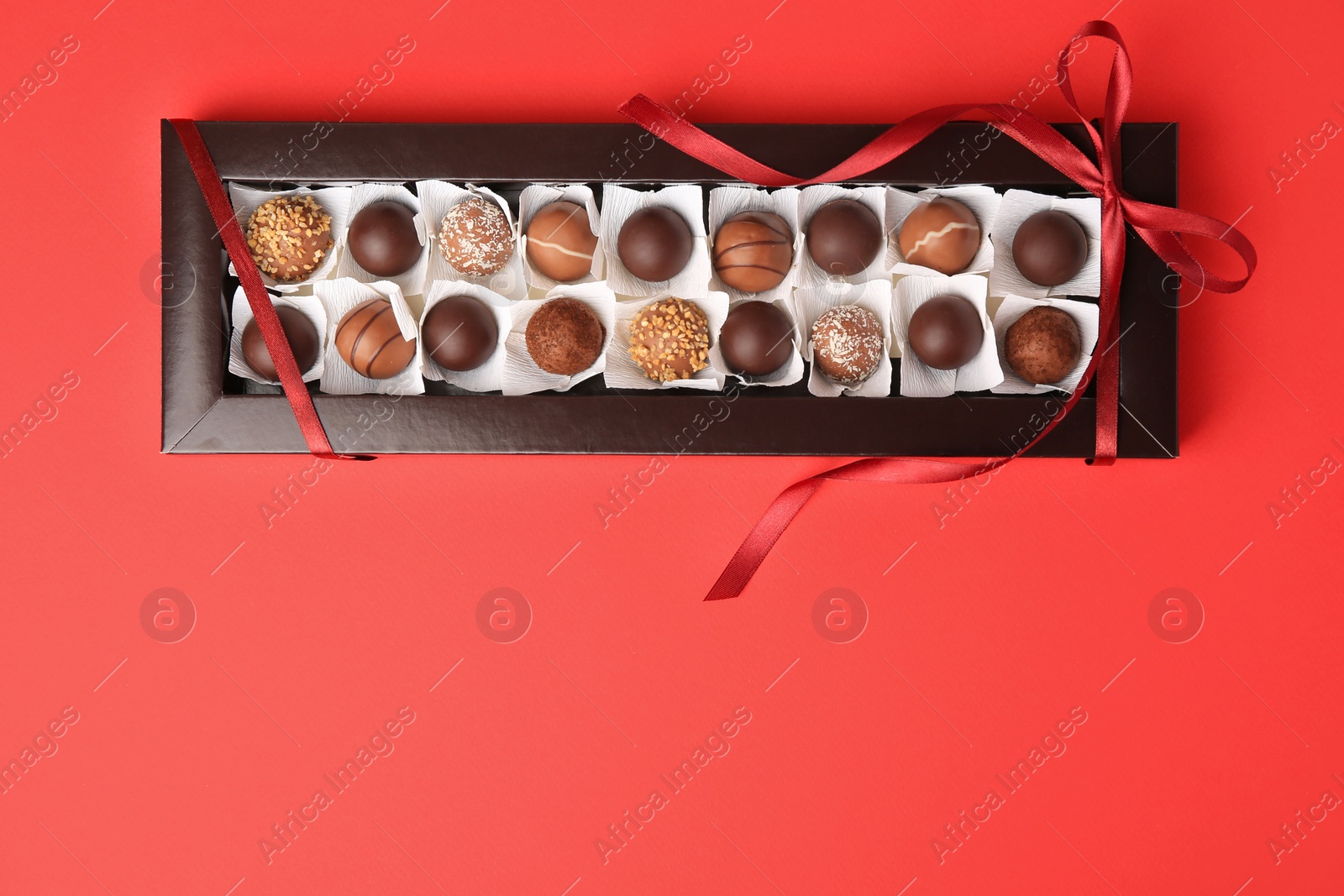 Photo of Box with delicious chocolate candies on red table, top view. Space for text