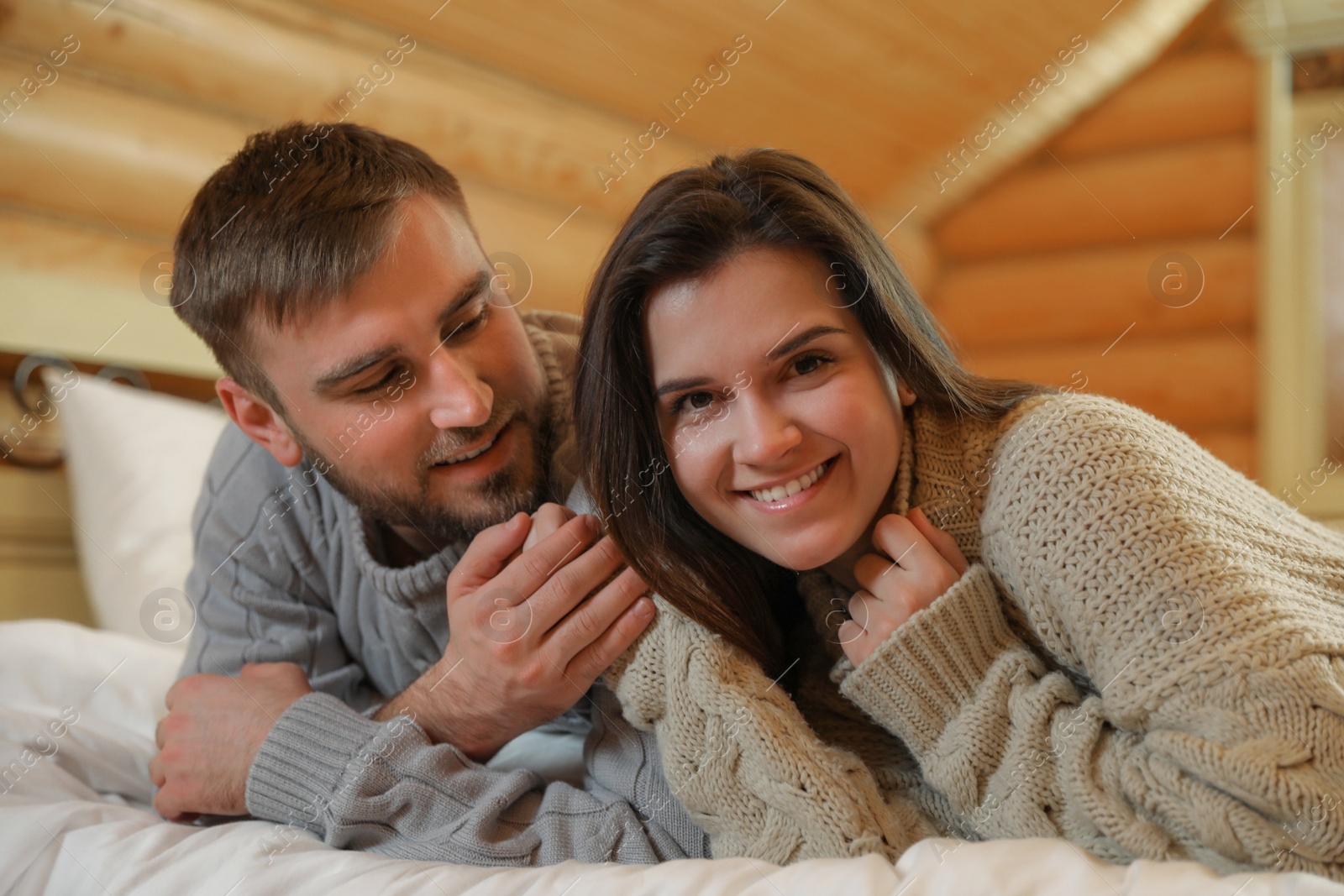 Photo of Young couple wearing warm sweaters on bed at home