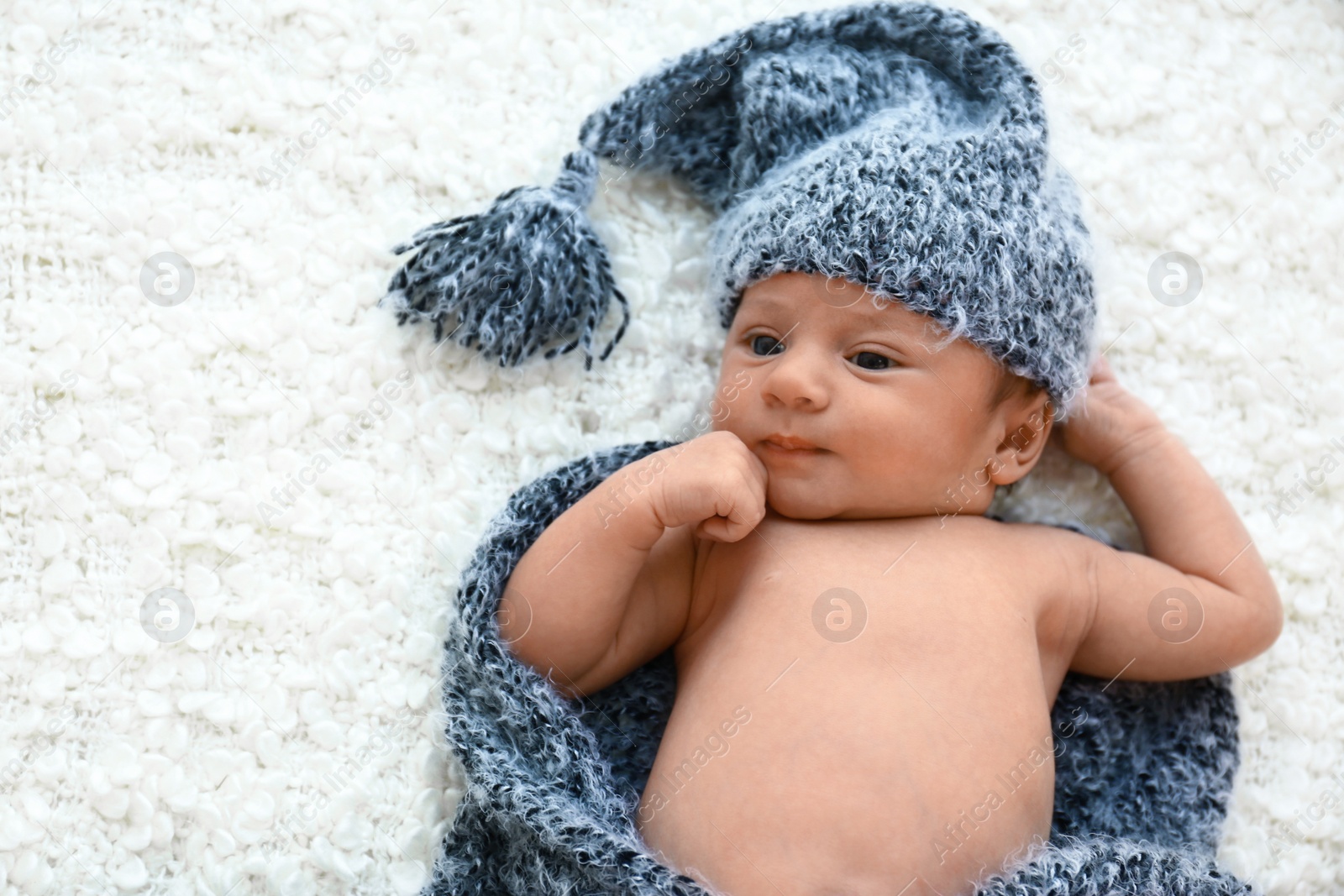 Photo of Cute little baby in grey hat and plaid lying on soft blanket, top view. Space for text