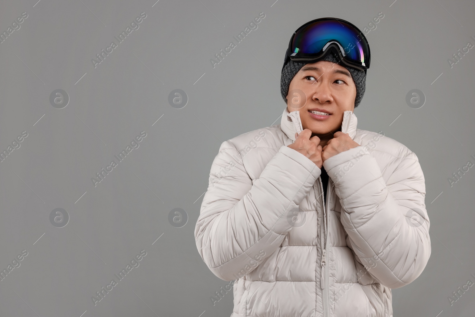 Photo of Winter sports. Man with ski goggles on grey background, space for text