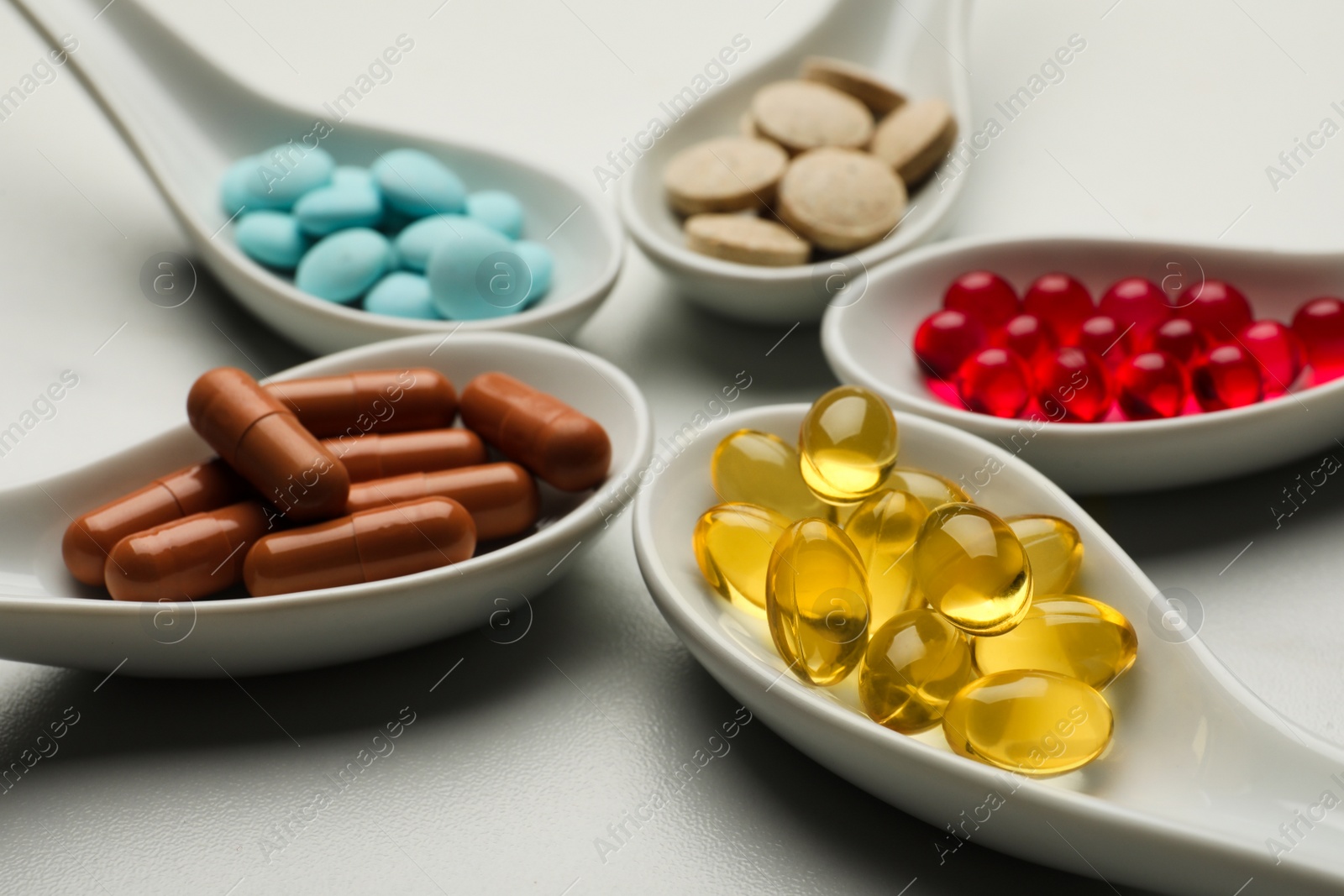 Photo of Spoons with different dietary supplements on white table, closeup