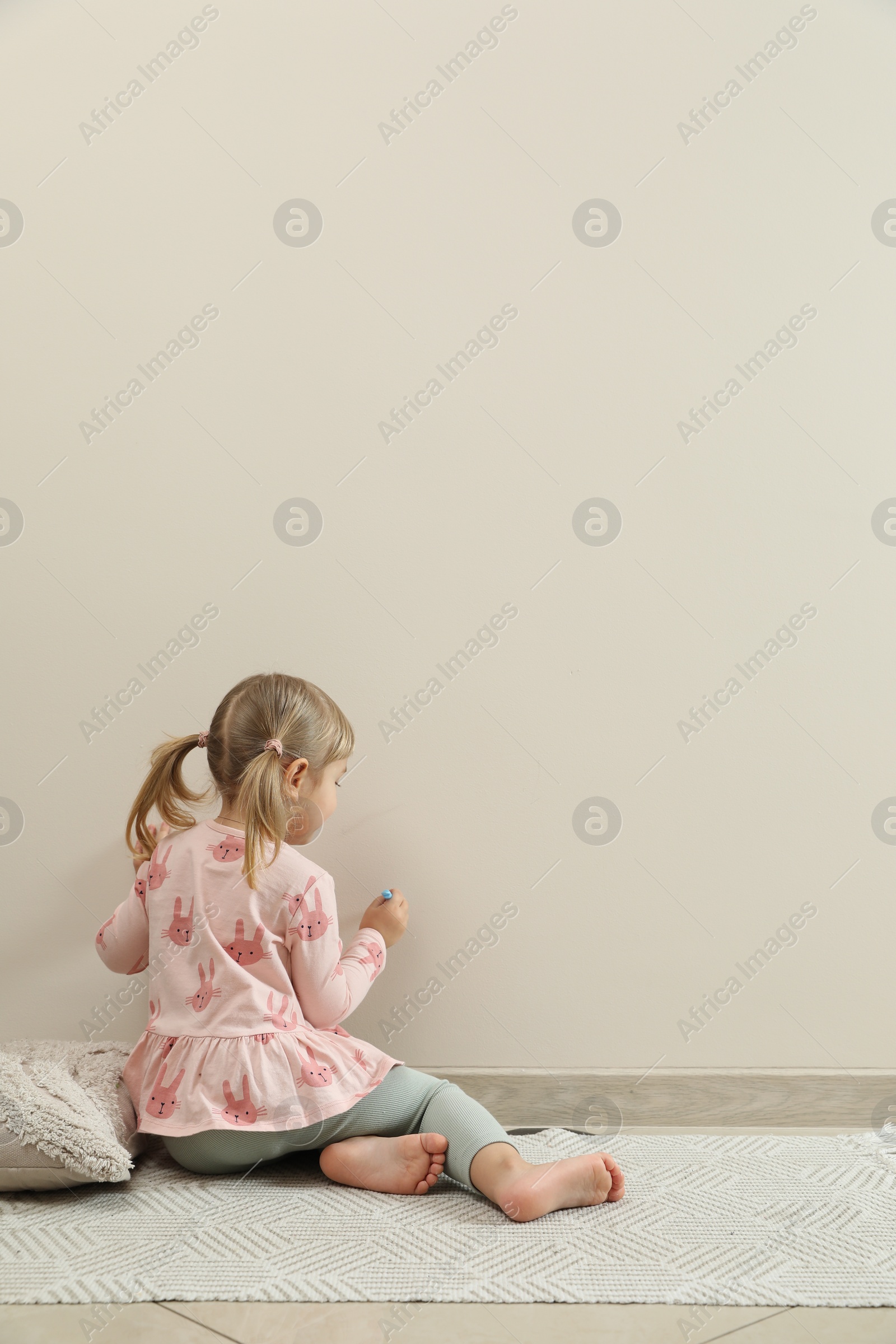 Photo of Little girl drawing on beige wall indoors, back view and space for text. Child`s art