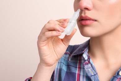 Photo of Woman using nasal spray on beige background, closeup. Space for text