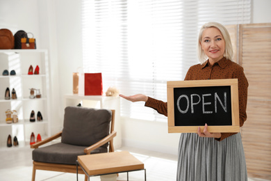 Photo of Female business owner holding OPEN sign in boutique. Space for text