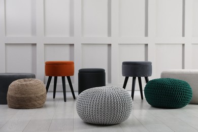 Different stylish poufs and ottomans near light wall