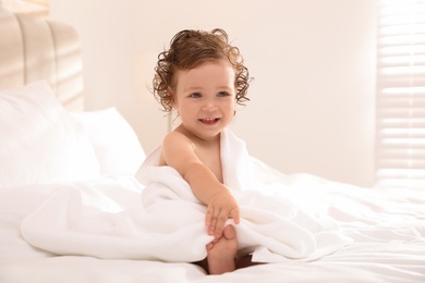 Cute little baby with soft towel on bed after bath