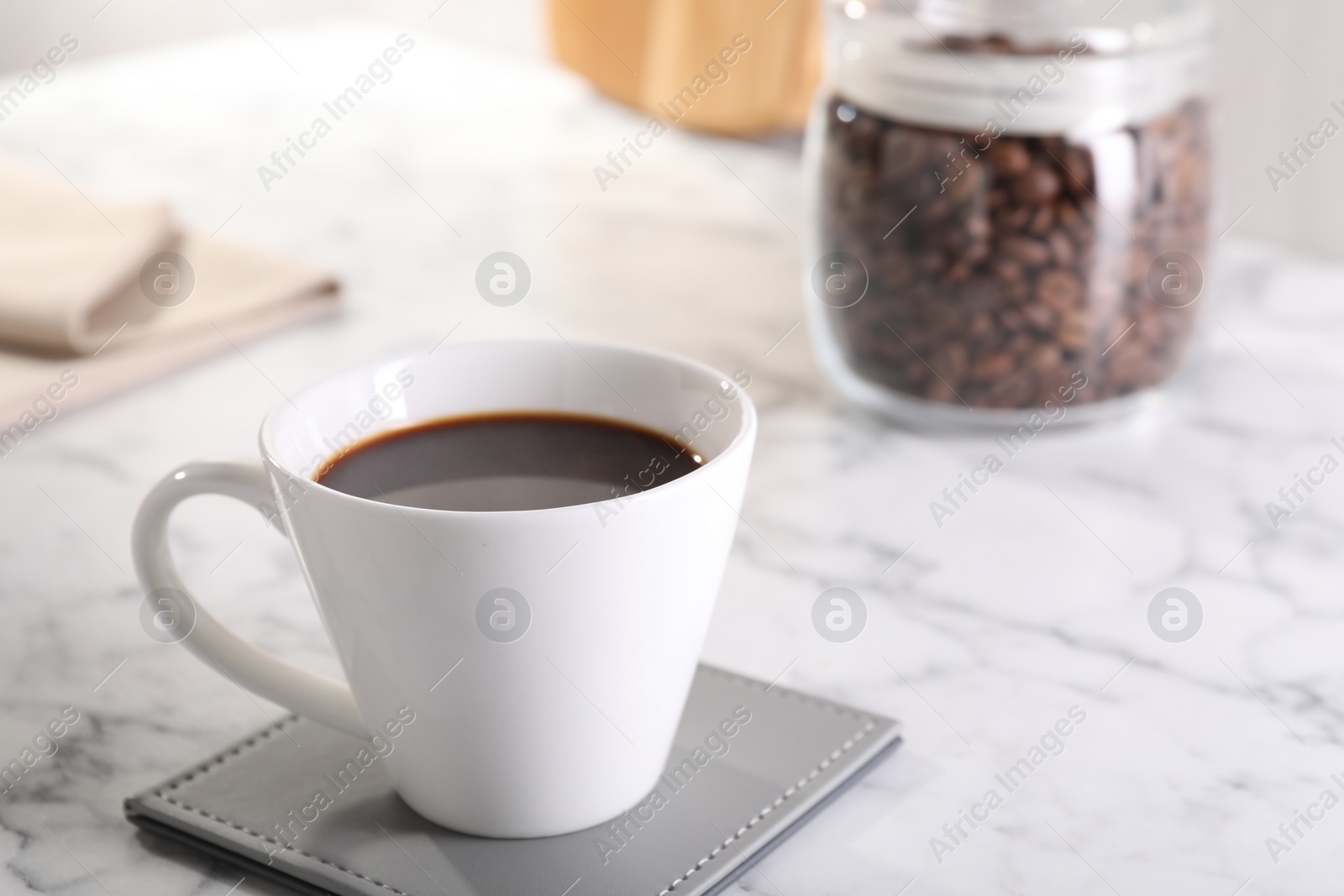Photo of Delicious coffee in cup on white marble table, closeup. Space for text