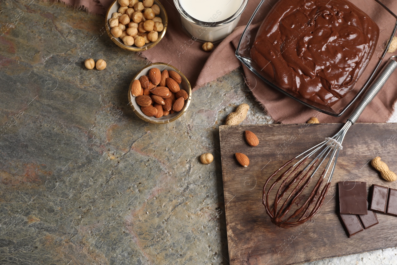 Photo of Bowl of chocolate cream, whisk and ingredients on textured table, flat lay. Space for text