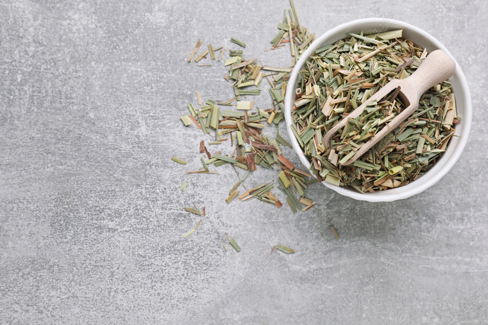 Photo of Bowl with aromatic dried lemongrass and scoop on light grey table, flat lay. Space for text