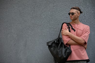 Photo of Handsome young man in stylish sunglasses and backpack near grey wall, space for text