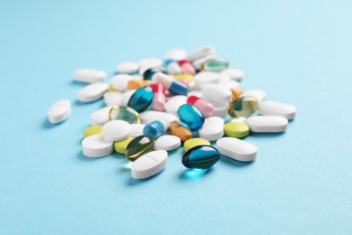Pile of different pills on light blue background, selective focus