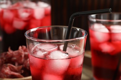 Glass of delicious iced hibiscus tea with straw against blurred background, closeup