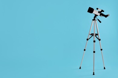 Tripod with modern telescope on light blue background, space for text