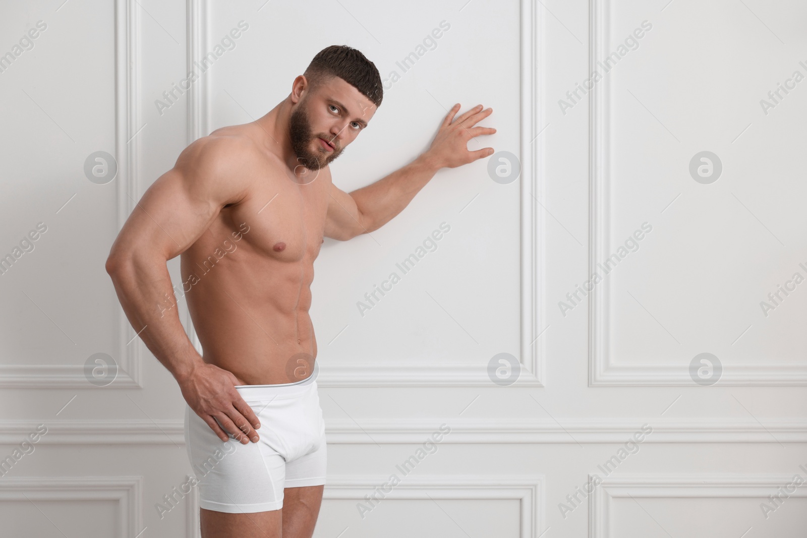 Photo of Young man in stylish underwear near white wall indoors. Space for text