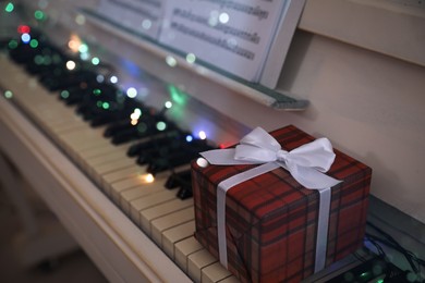 Photo of Gift box and fairy lights on piano keys indoors, space for text. Christmas music