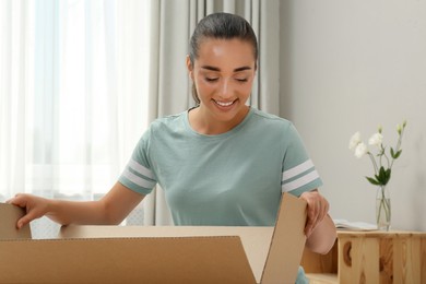 Happy young woman opening parcel at home. Internet shopping