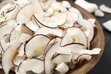 Photo of Tasty coconut chips in wooden bowl, closeup