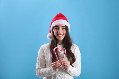 Photo of Beautiful woman in Santa Claus hat making heart with candy canes on light blue background