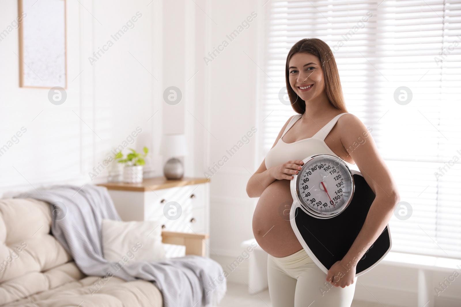 Photo of Young pregnant woman with scales at home. Space for text