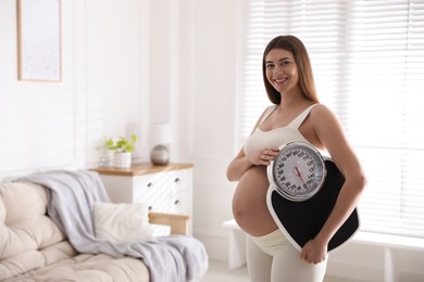 Photo of Young pregnant woman with scales at home. Space for text