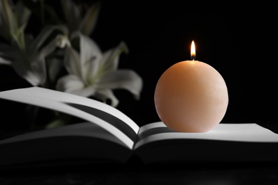 Burning candle and book on table in darkness. Funeral symbol