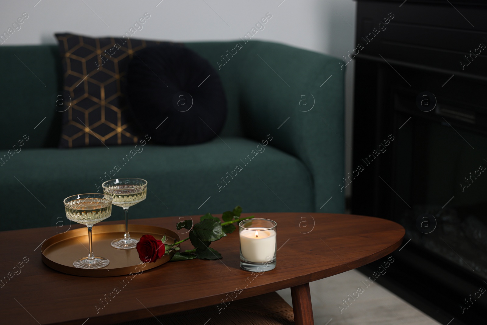 Photo of Burning candle, glasses of wine and beautiful red rose on wooden table in room