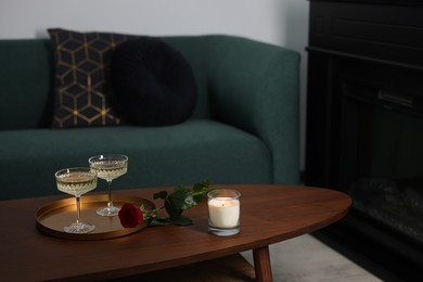 Burning candle, glasses of wine and beautiful red rose on wooden table in room