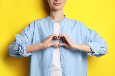 Photo of Woman making heart with hands on yellow background, closeup