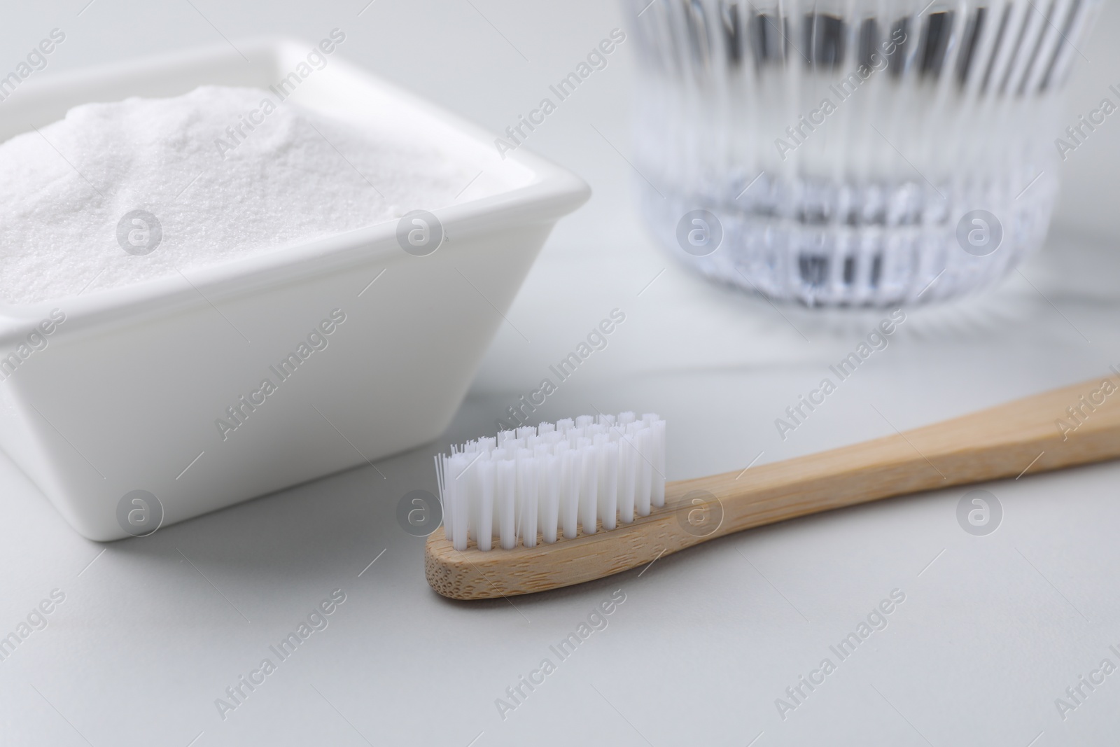Photo of Bamboo toothbrush and bowl of baking soda on white table, closeup