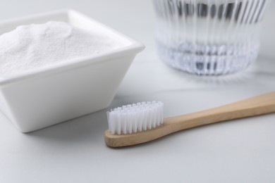 Bamboo toothbrush and bowl of baking soda on white table, closeup